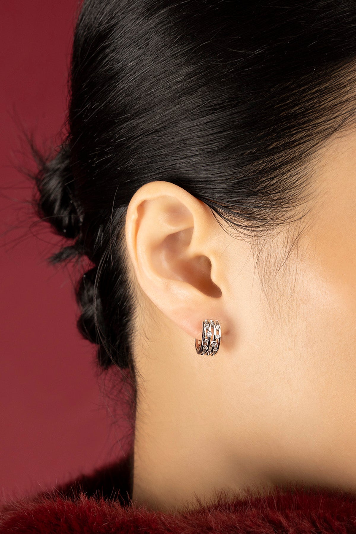 Woman wearing APM Hoop Earrings, a quiet sparkle against deep crimson.