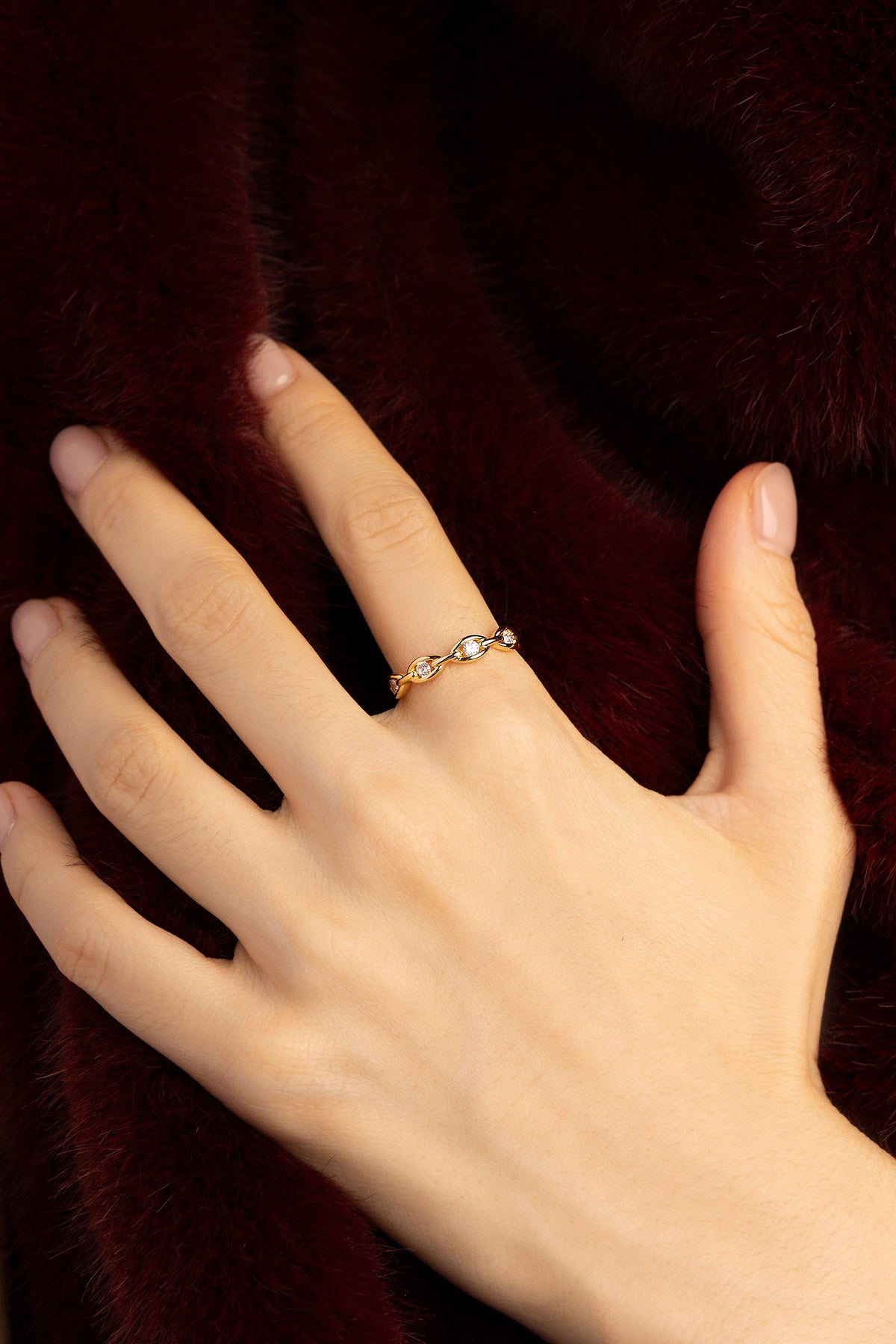Woman wearing APM Ring, a delicate golden whisper against plush burgundy.