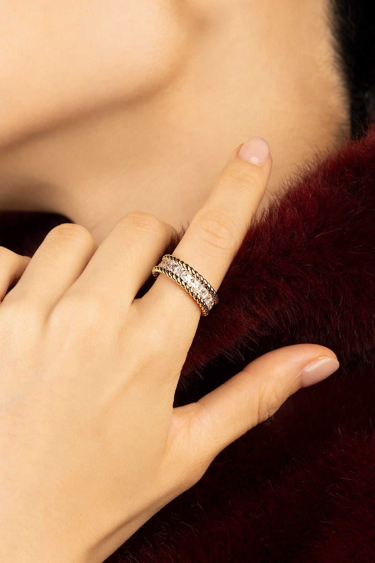 Woman wearing APM ring, twisted golden band framing quiet sparkle, effortlessly refined.