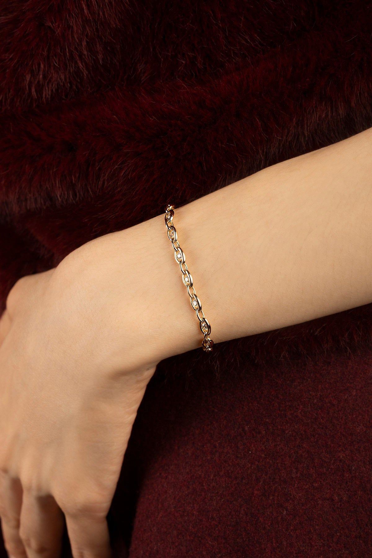 Woman wearing an APM chain bracelet, a golden whisper against burgundy warmth.