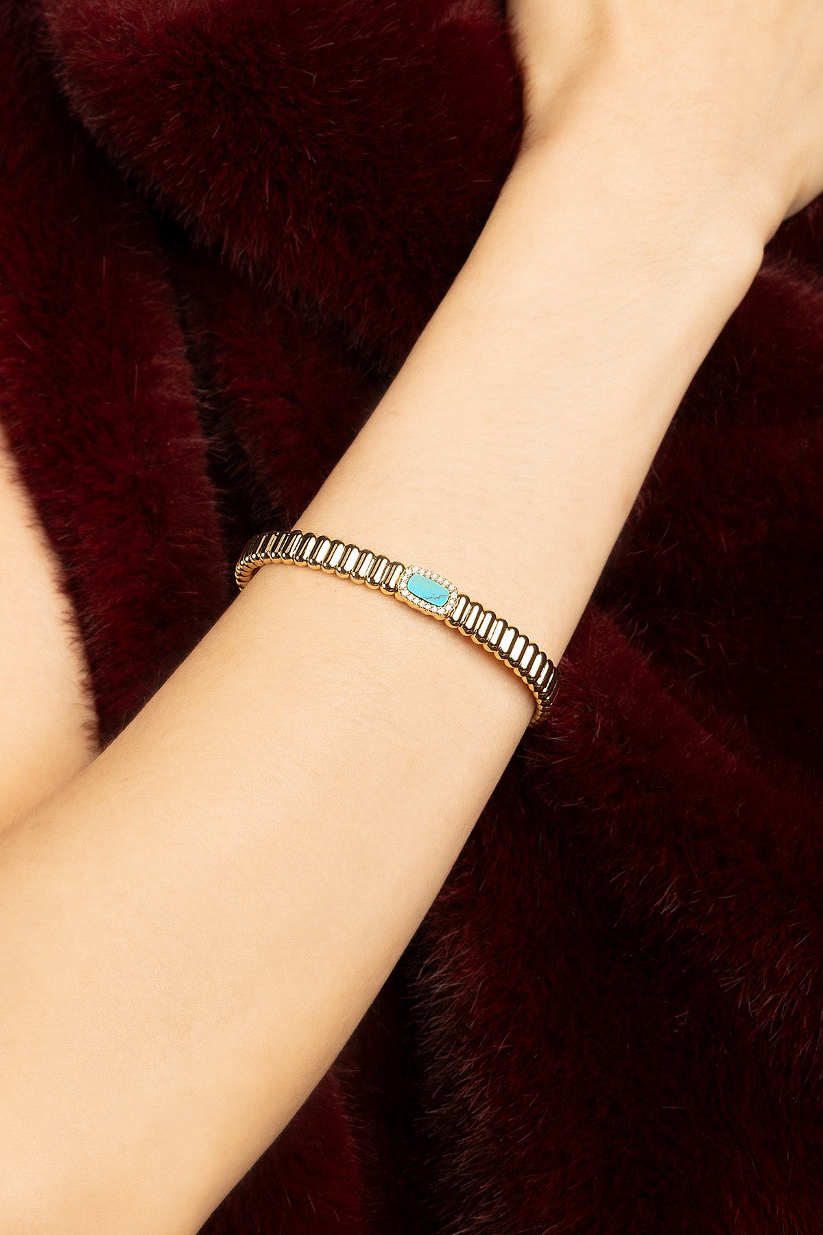 Woman wearing APM bracelet, a golden ripple with turquoise charm, effortlessly chic.