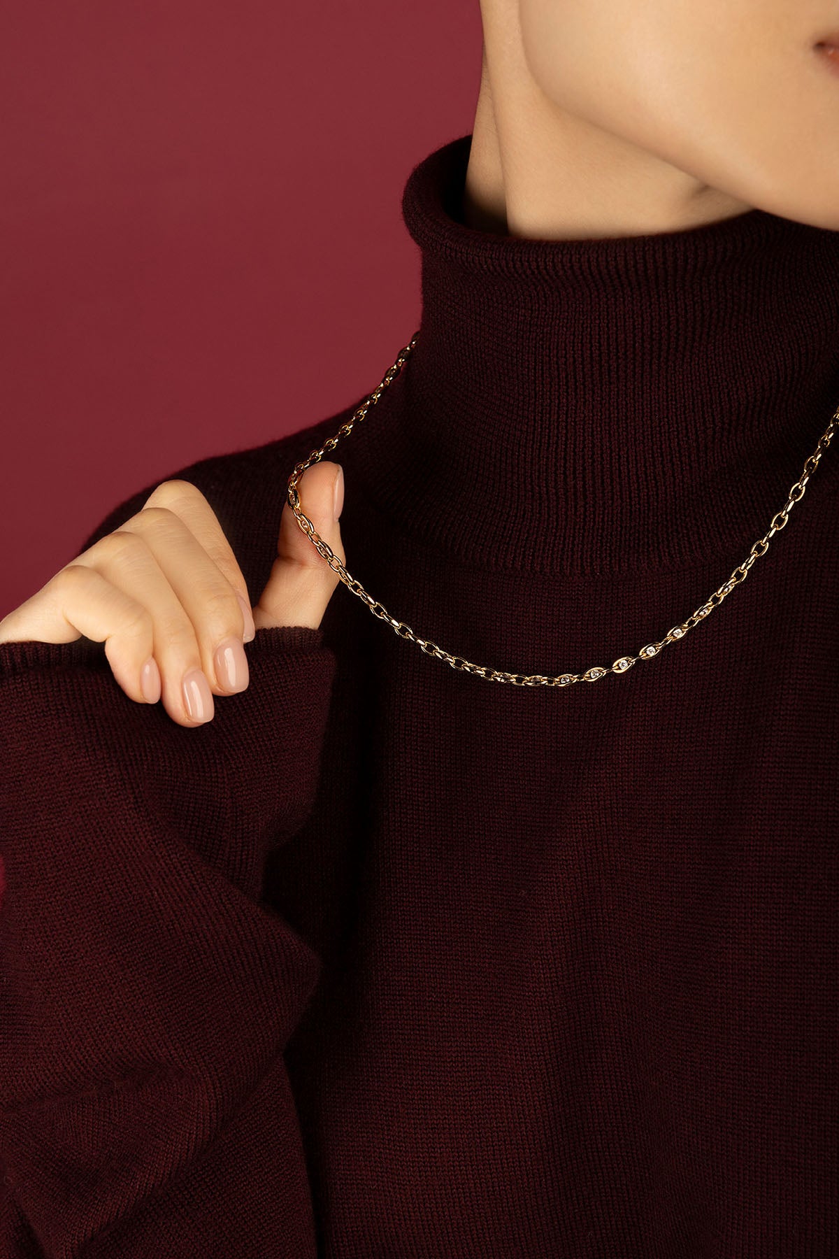 Woman wearing APM Monaco chain necklace, a golden whisper over burgundy warmth.
