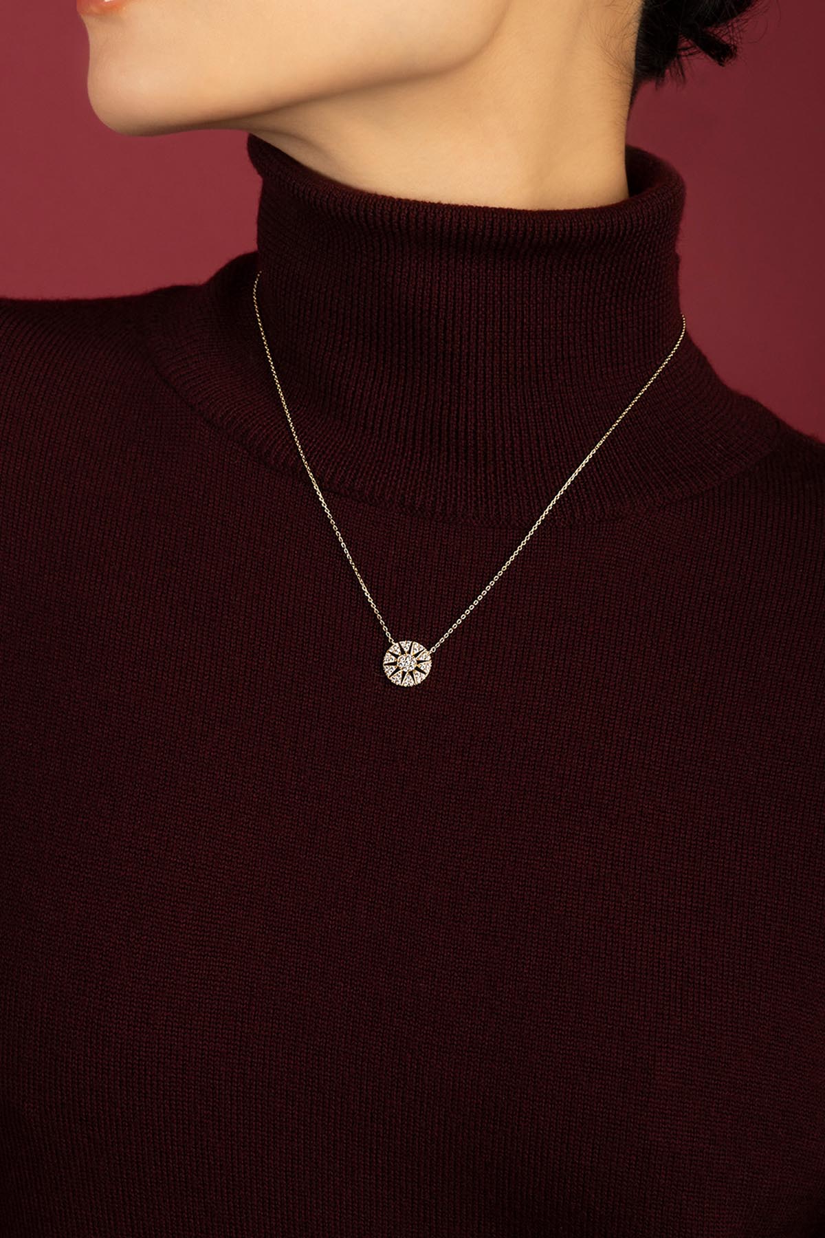 Woman wearing APM Rose des Vents Necklace, a radiant charm against burgundy warmth.