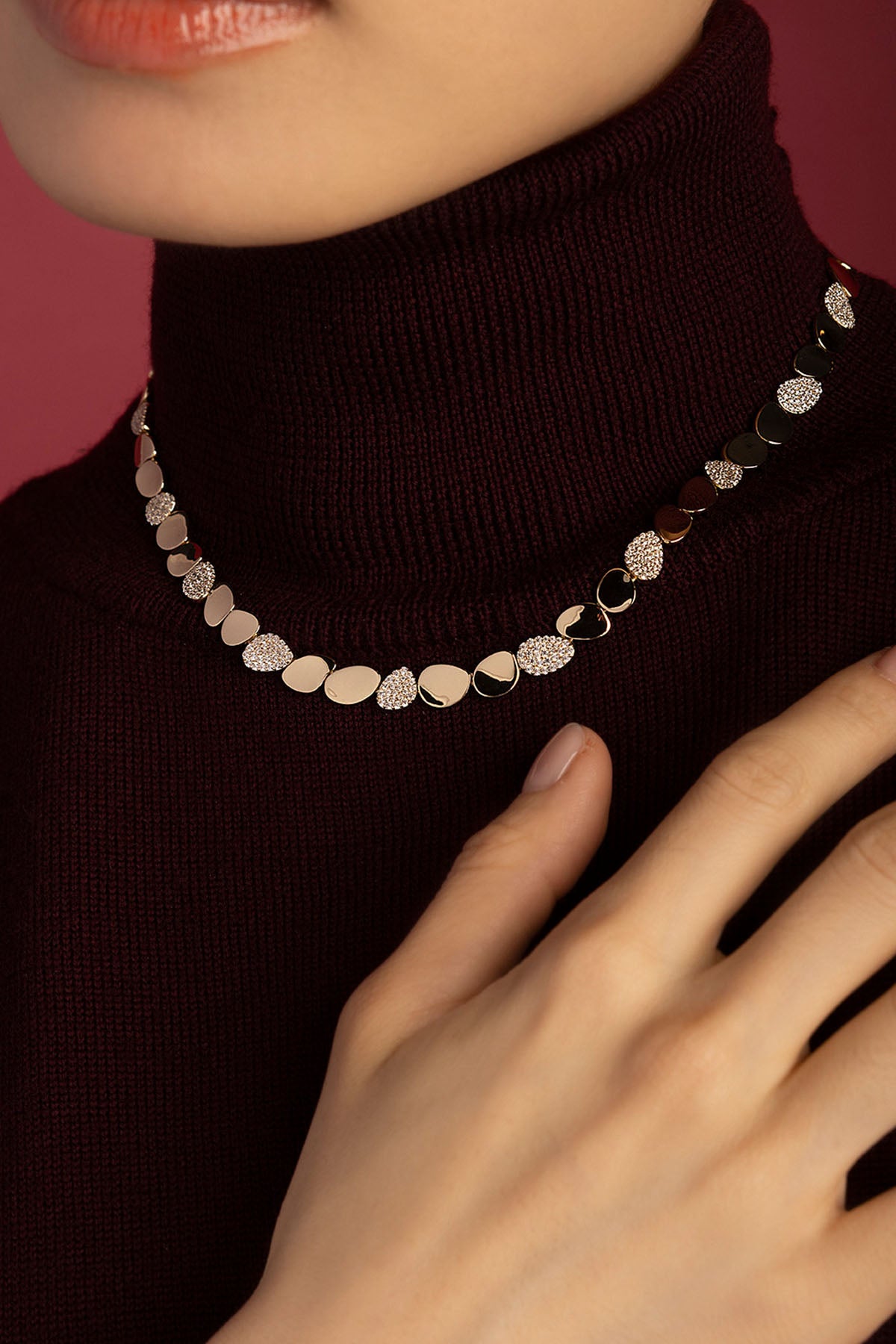 Woman wearing APM Monaco necklace, a pebbled glow against burgundy warmth.