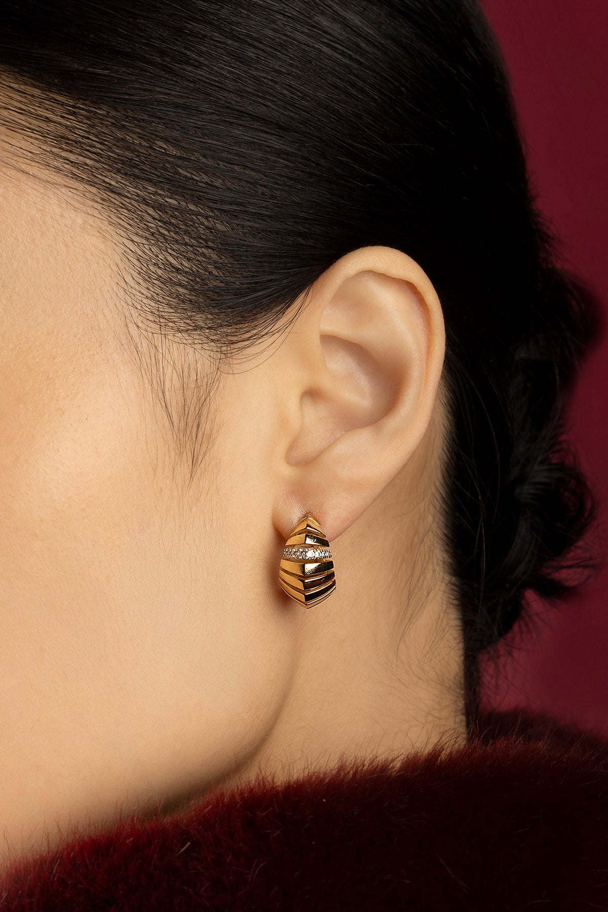 Woman wearing APM Monaco earrings, sculpted golden curves whispering quiet elegance.