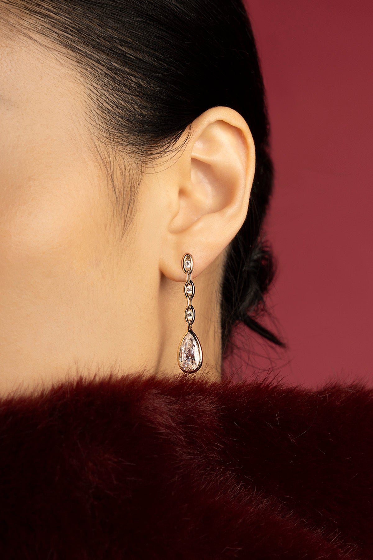 Woman wearing APM drop earrings, a whisper of crystal elegance against crimson.