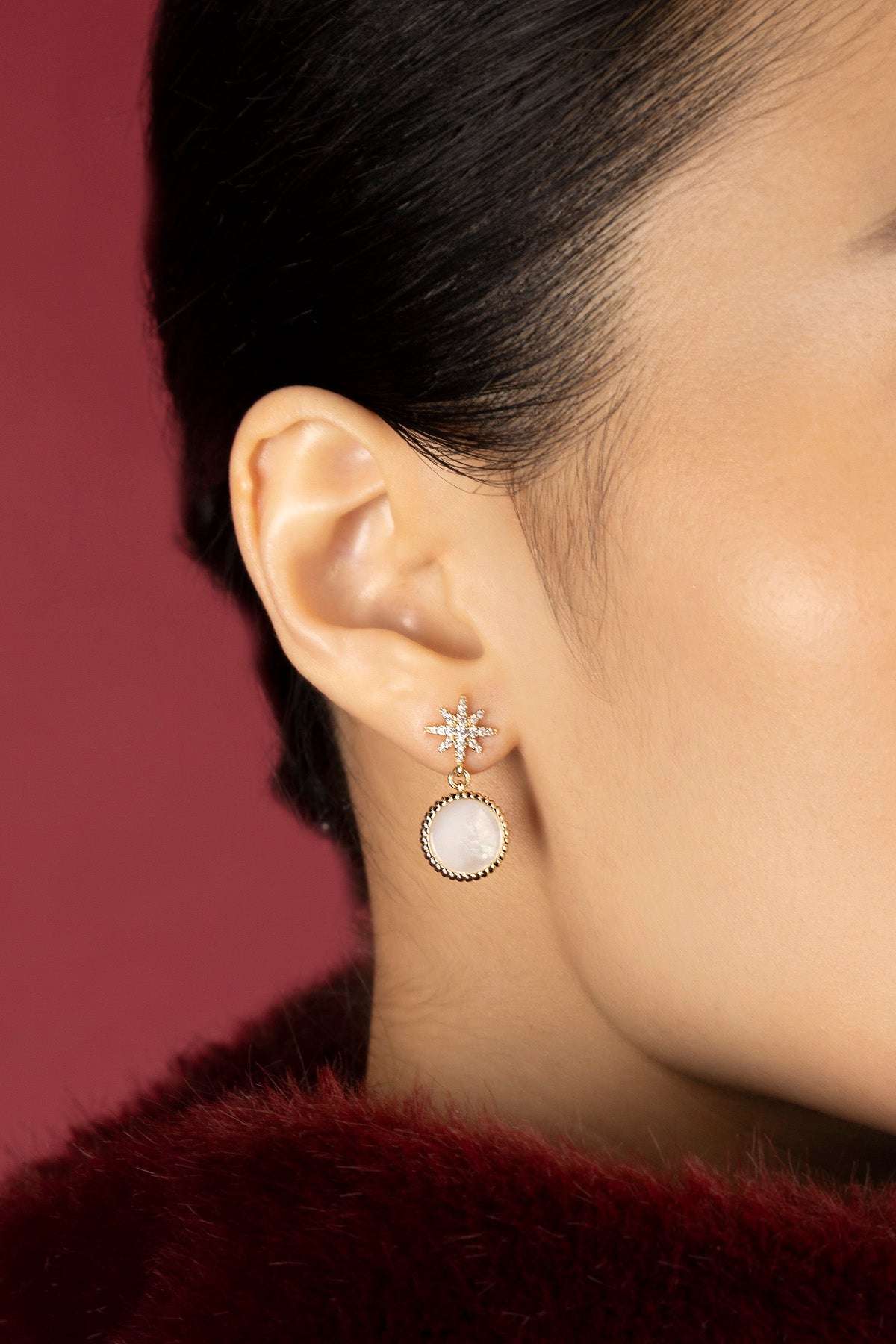 Woman wearing APM star drop earrings, a celestial glow against crimson warmth.