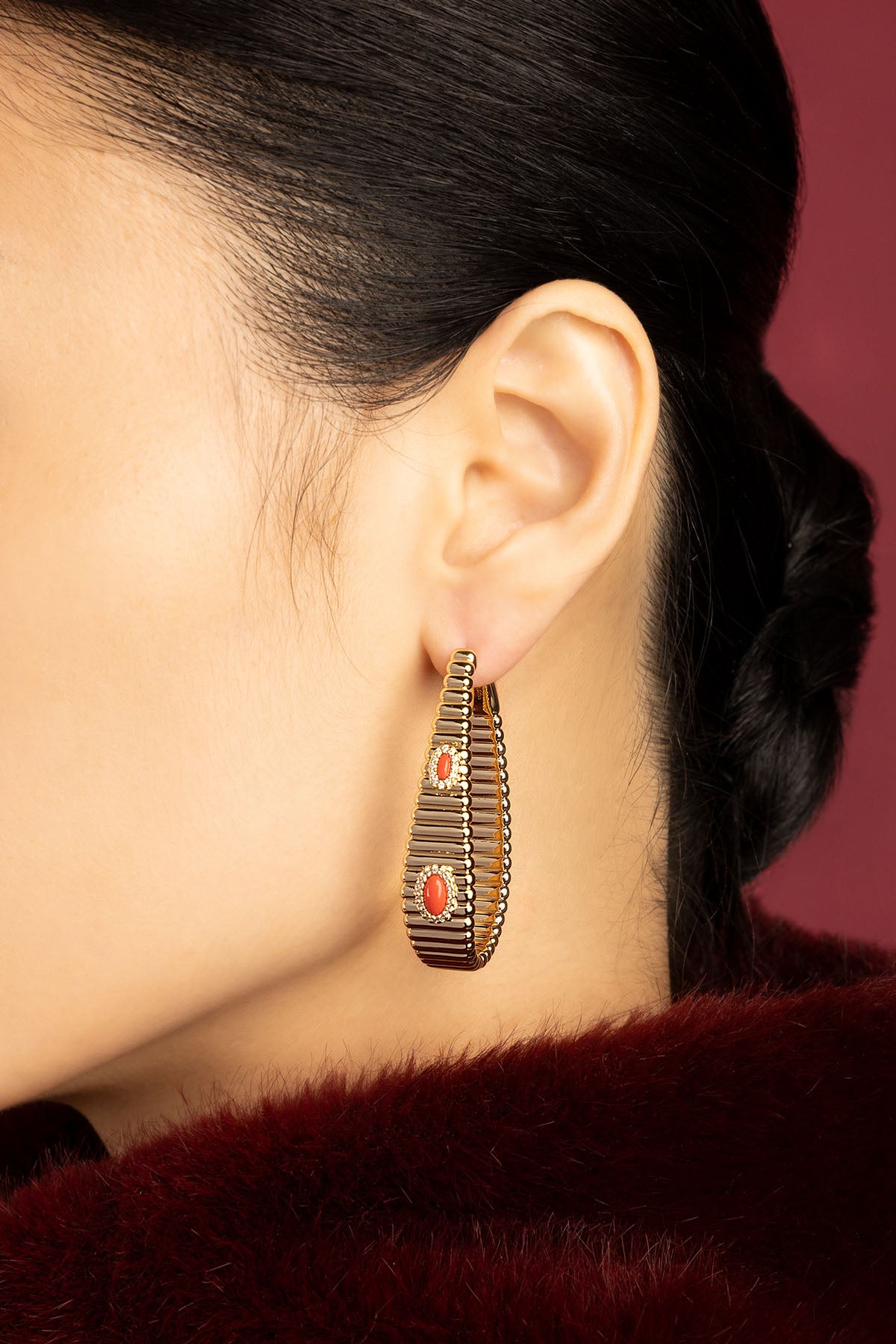Woman wearing APM ribbed hoop earrings, coral accents glowing with quiet warmth.