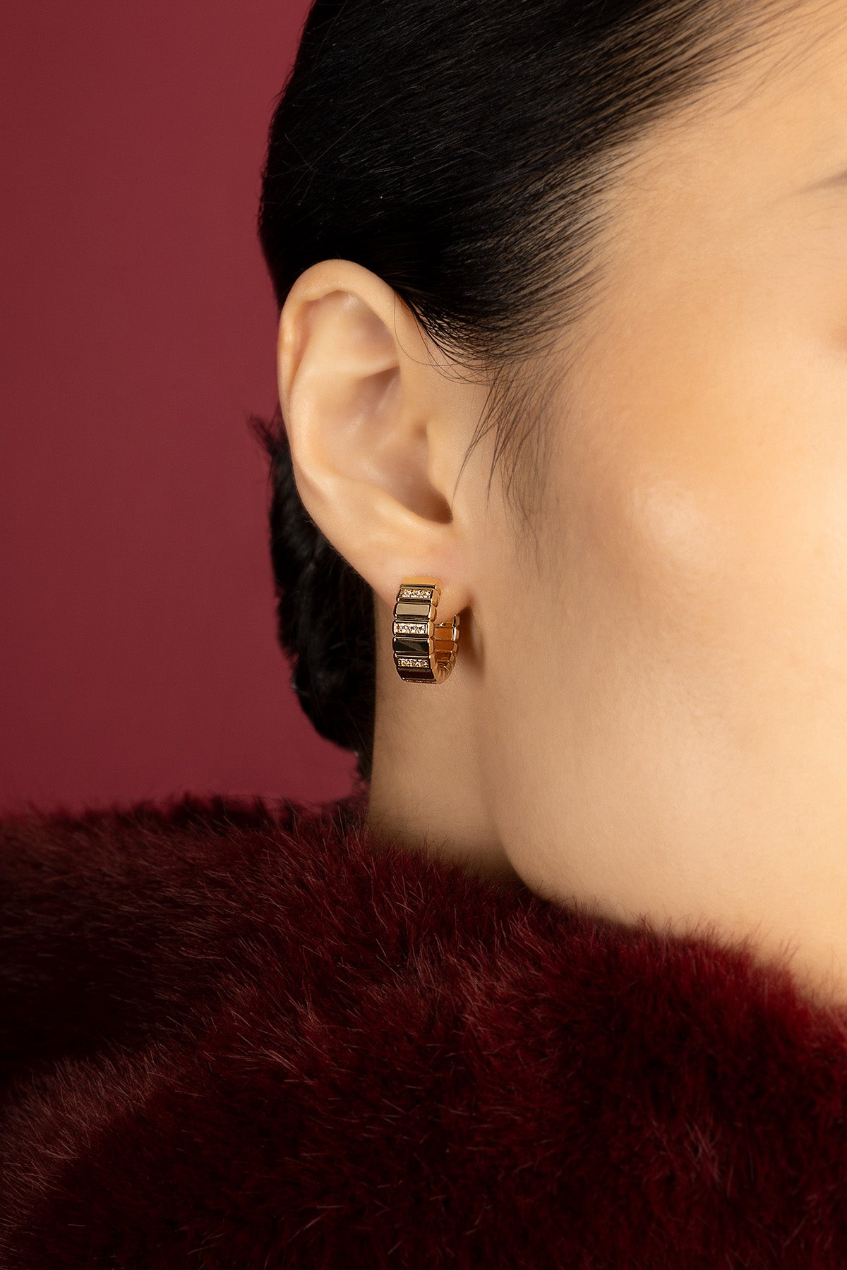 Woman wearing APM Hoop Earrings, a golden whisper against crimson warmth.