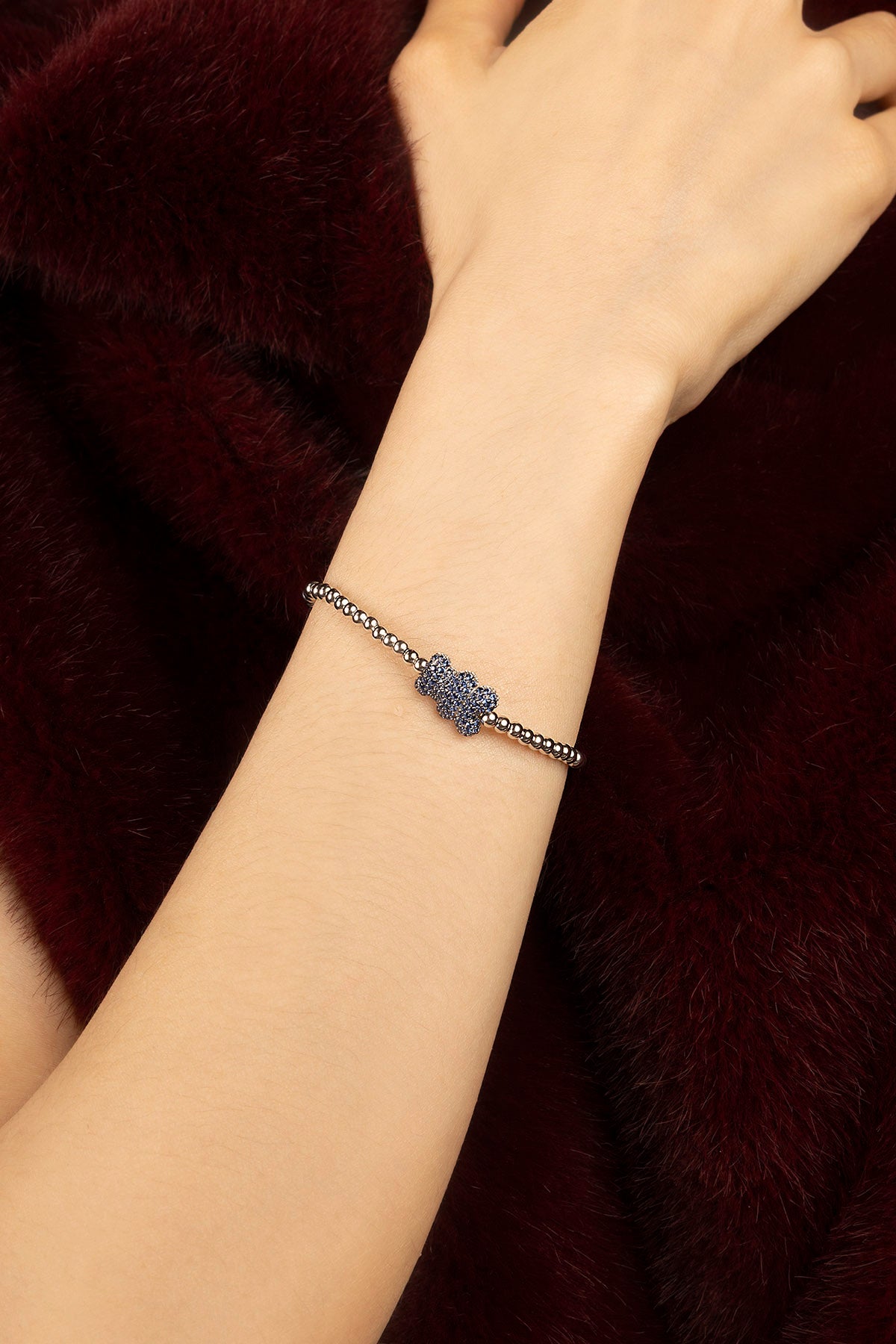 Woman wearing APM beaded bracelet, a delicate bloom of blue against burgundy fur.