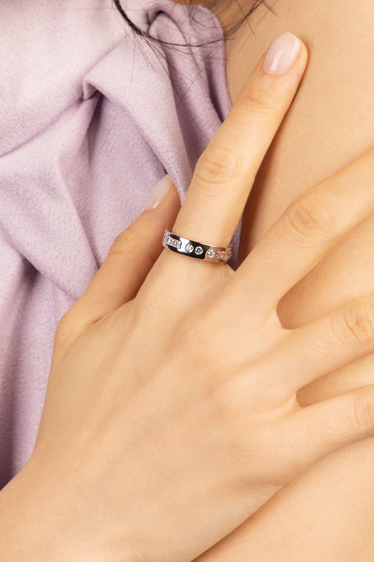 Hand wearing a ring with small stones, against a soft pink fabric background