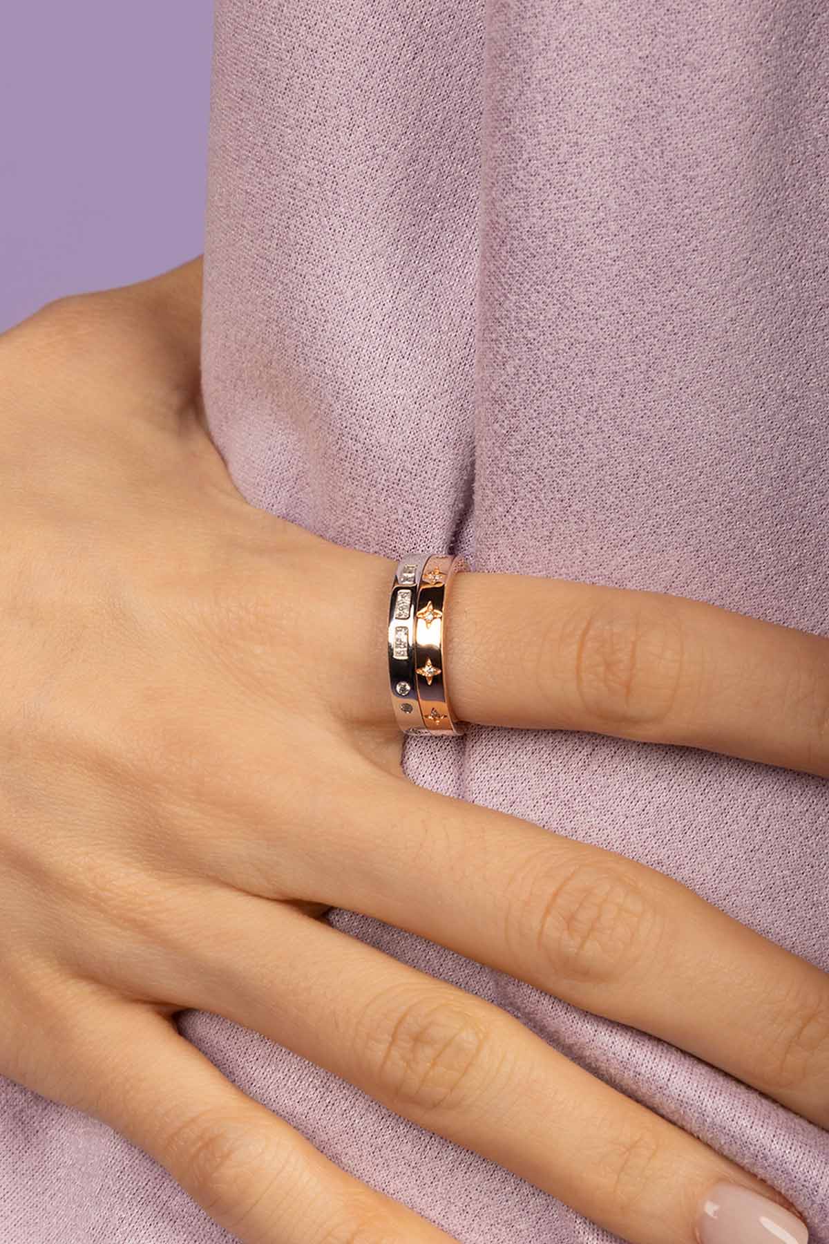 Hand wearing a stack of two rings on a light purple background