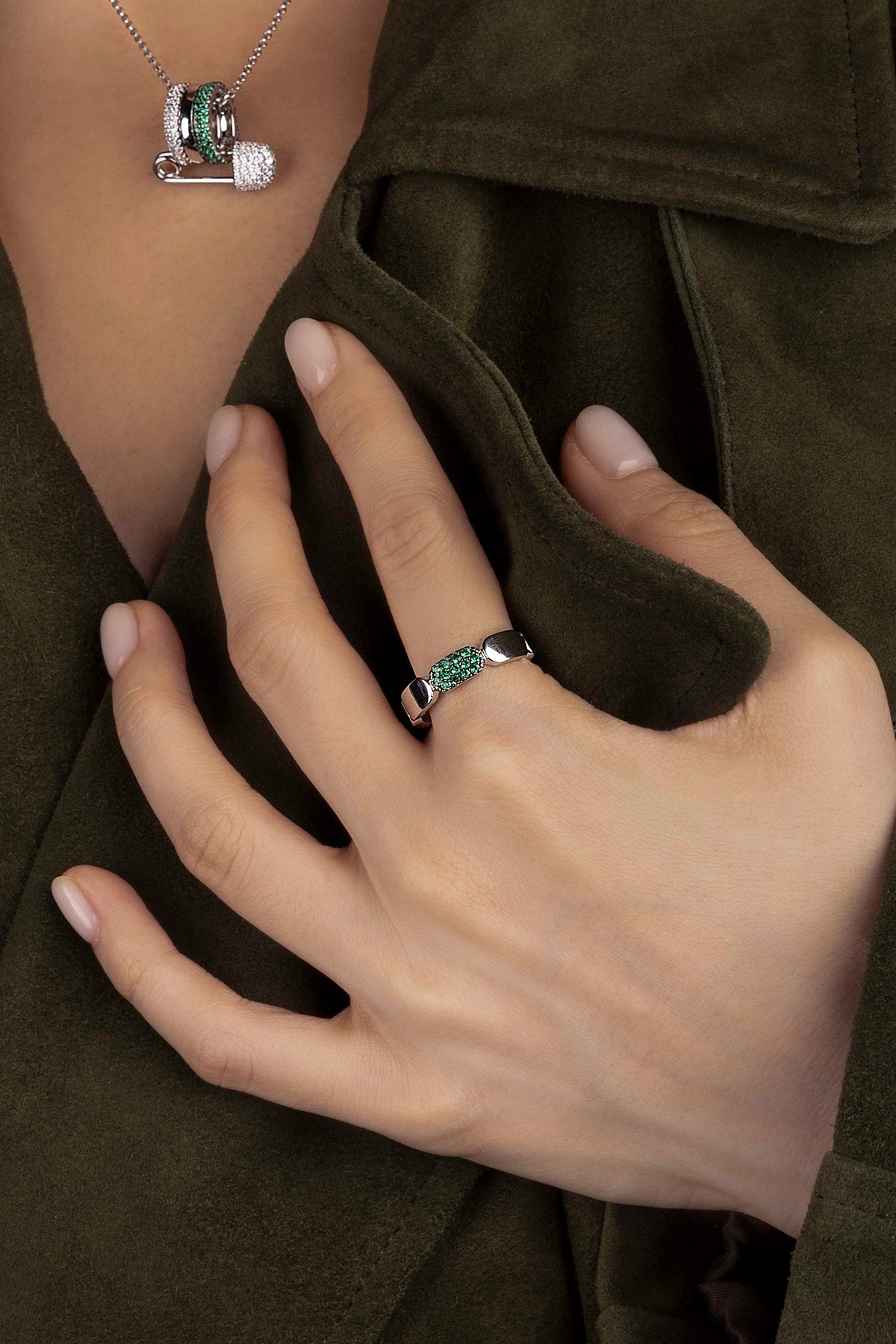 Close-up of a hand wearing a ring with green stones against a brown fabric background.