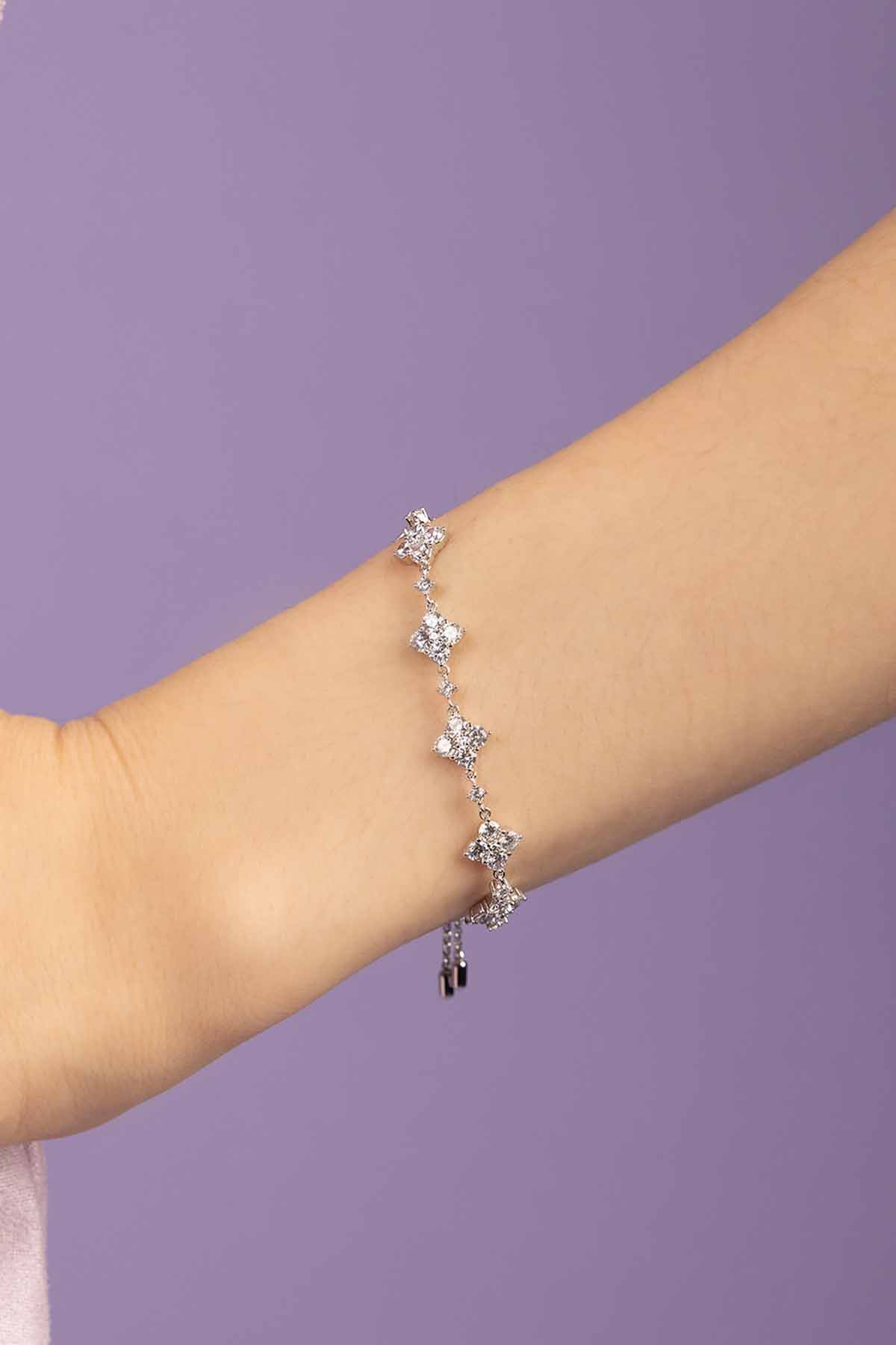 Silver bracelet with floral charms on a person's wrist against a purple background