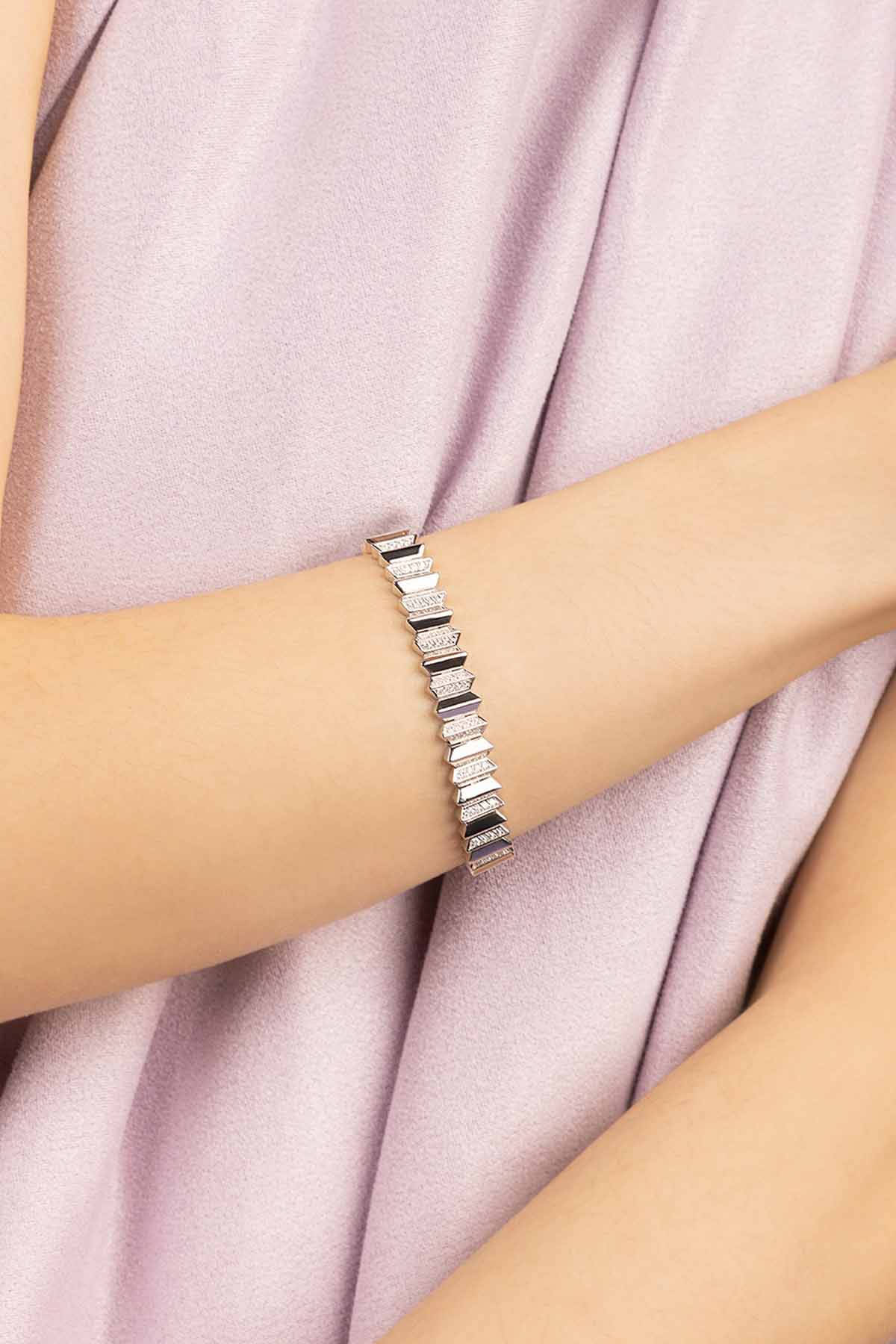 Silver bracelet on a person's wrist with a soft pink fabric background