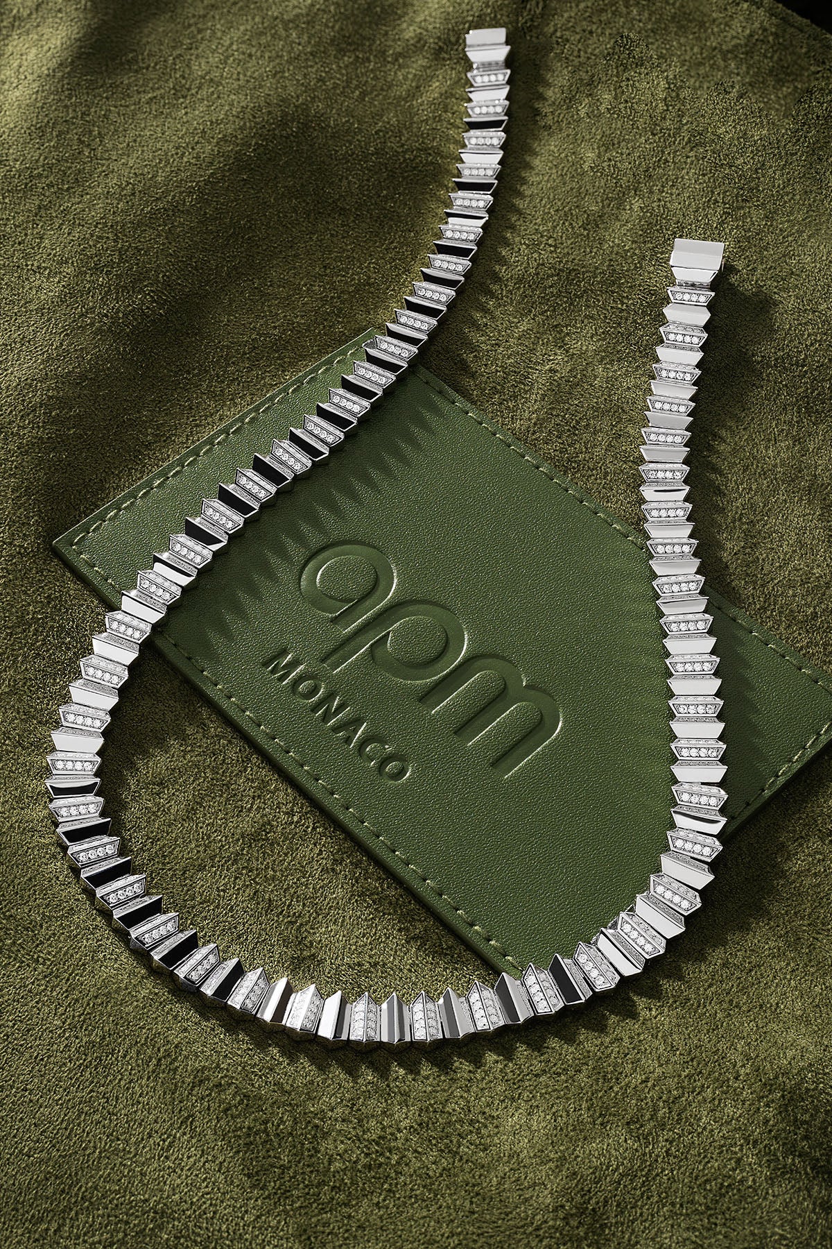 Silver necklace on a green textured surface with 'qpm Monaco' logo
