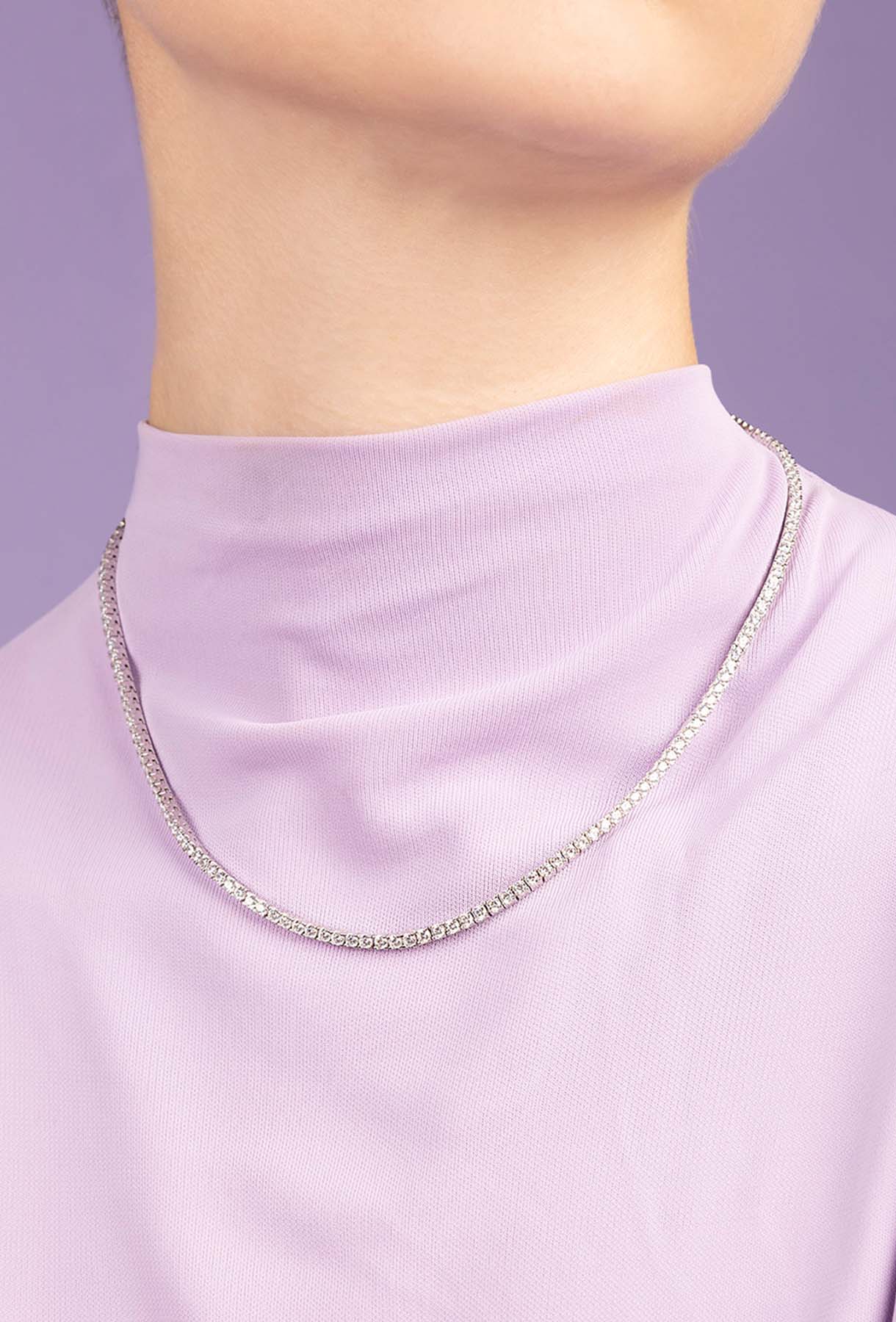 Silver chain necklace on a person wearing a light purple top against a purple background