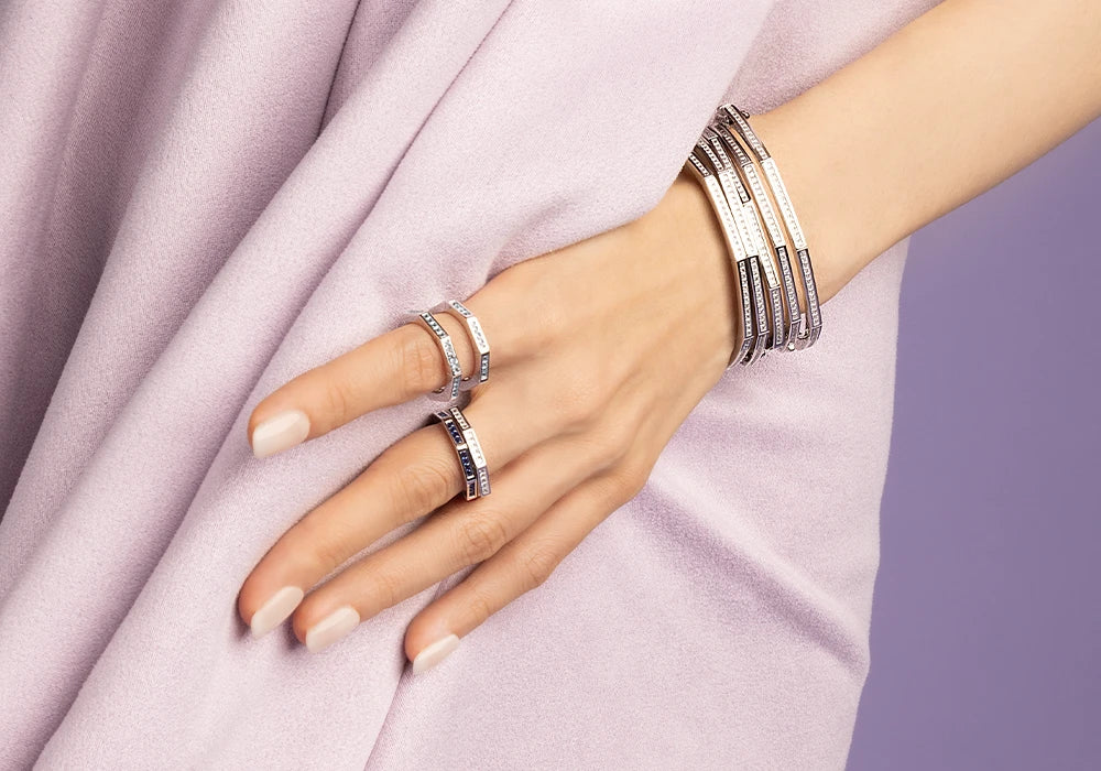 Hand wearing multiple APM MONACO Printemps Lumiere silver rings and bracelets on a light purple fabric background