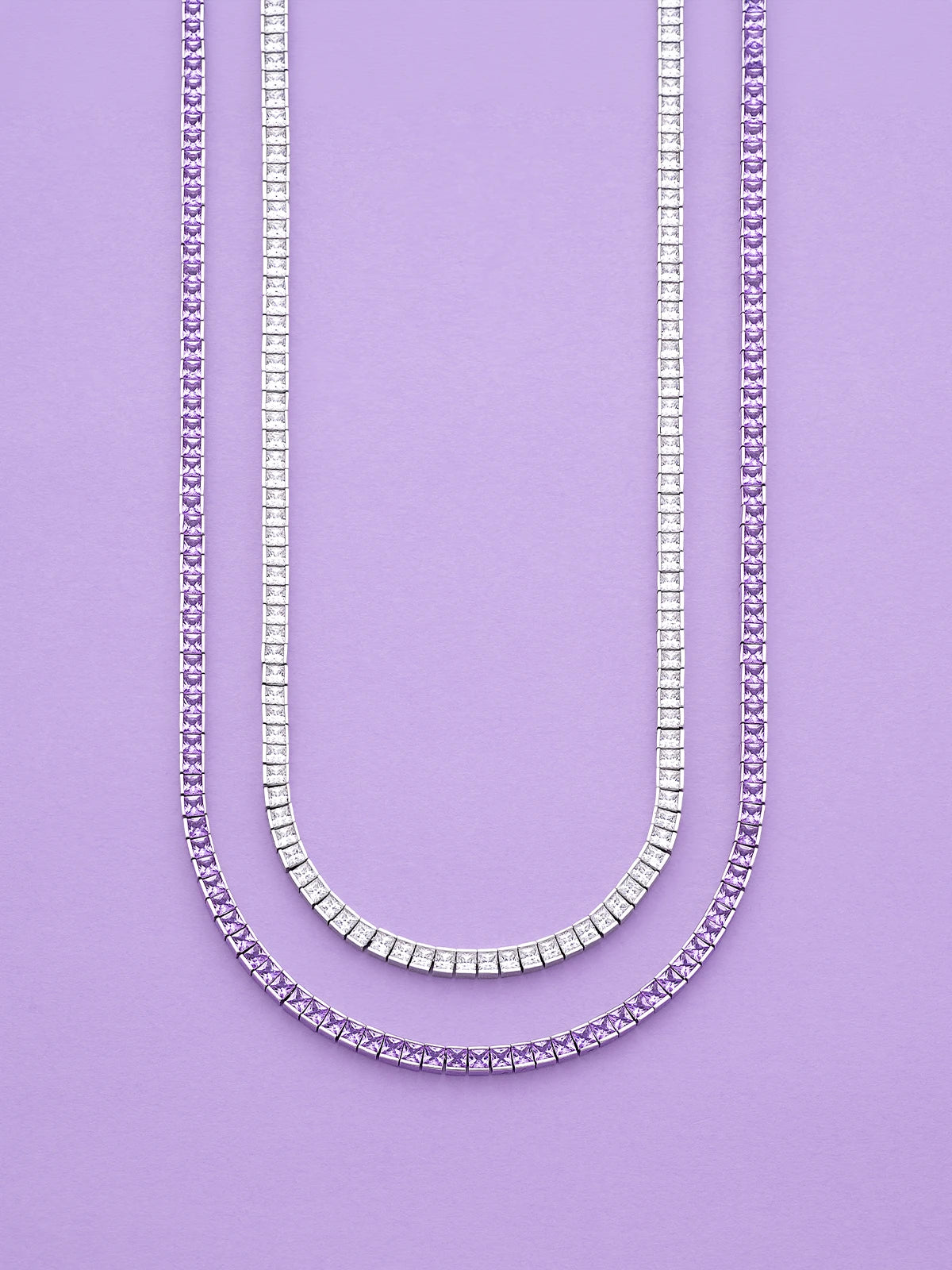 Two APM MONACO Printemps necklaces in silver and purple on a purple background
