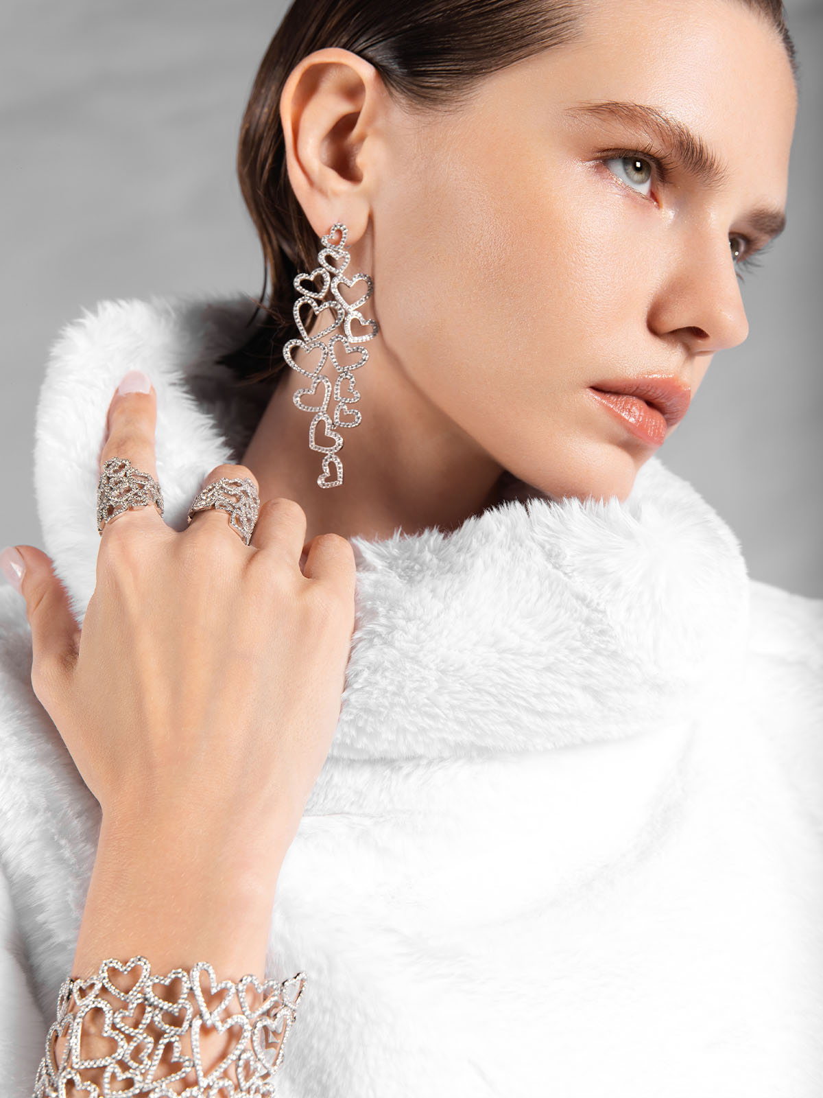 Woman wearing silver earrings, ring, and bracelet from APM MONACO against a gray background