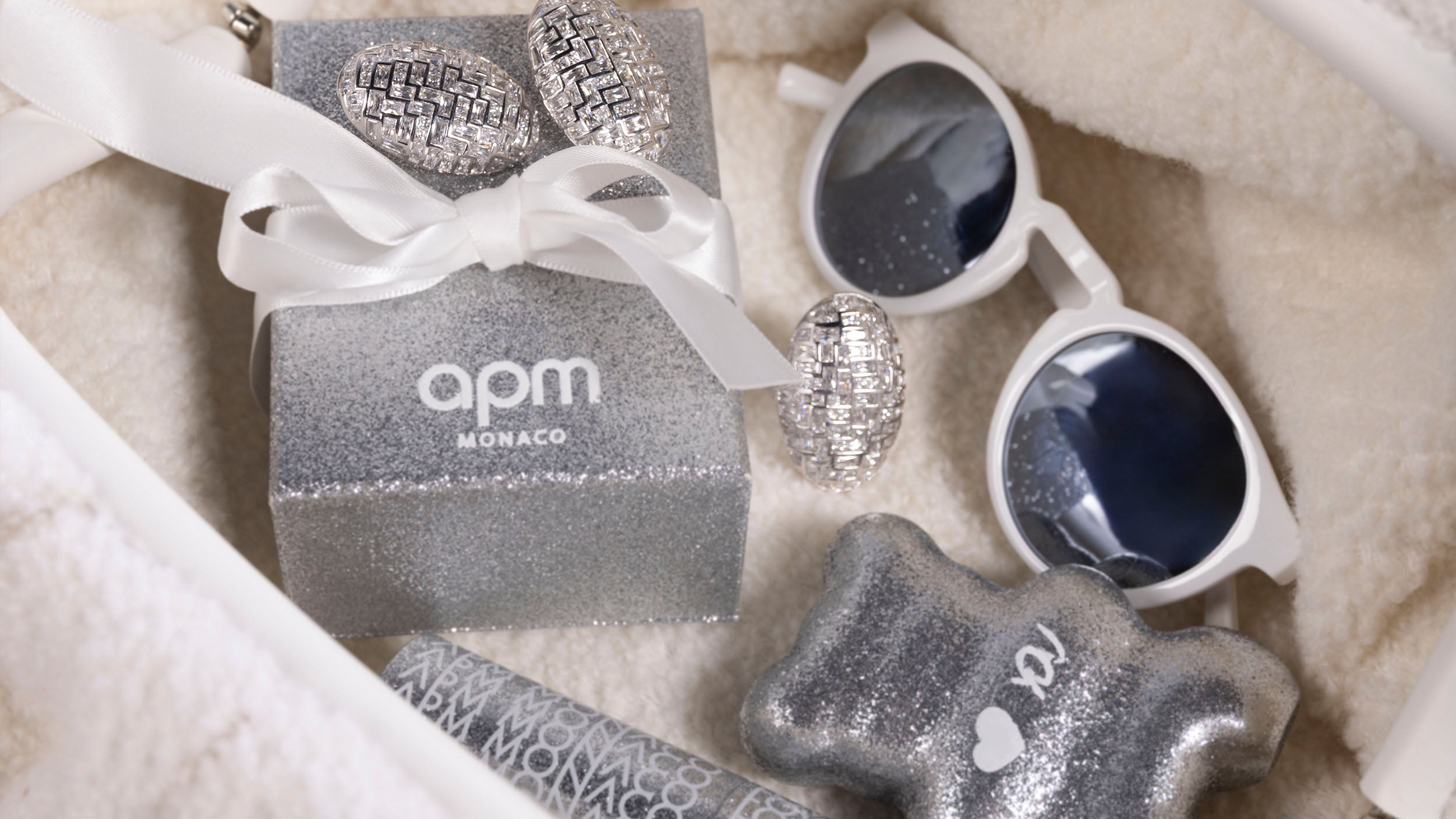 Silver jewelry set with 'APM MONACO' packaging on a soft surface