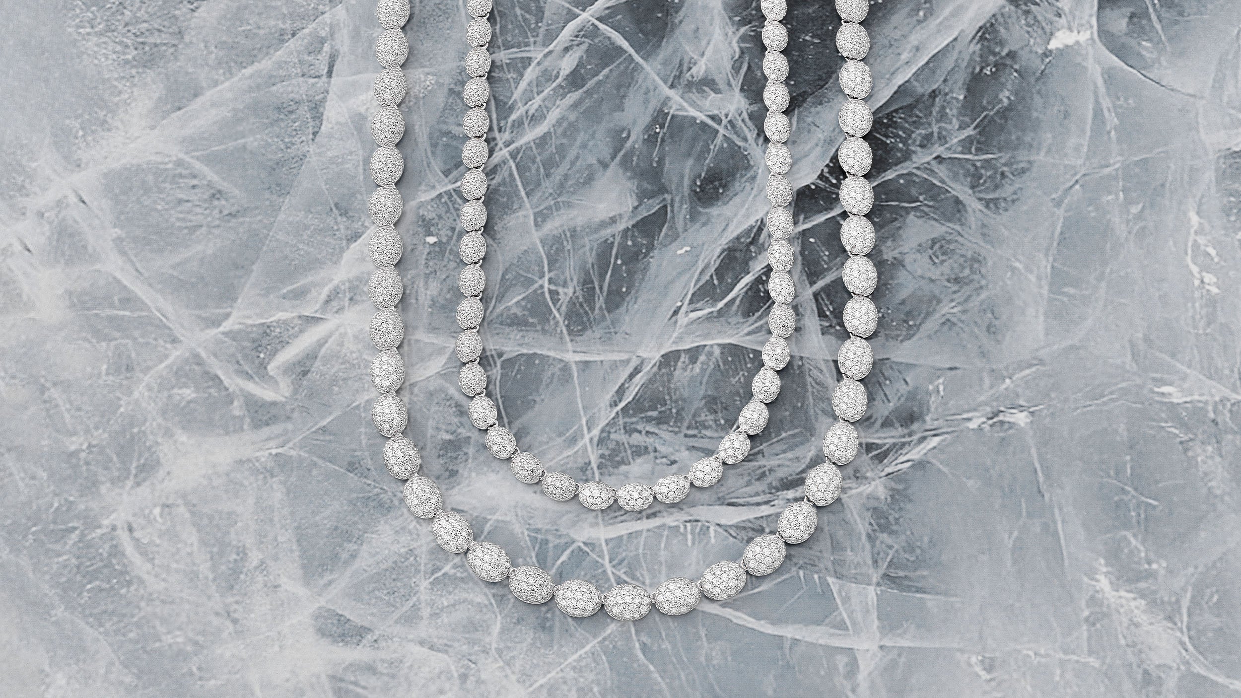 Two APM MONACO silver necklaces on a textured gray surface