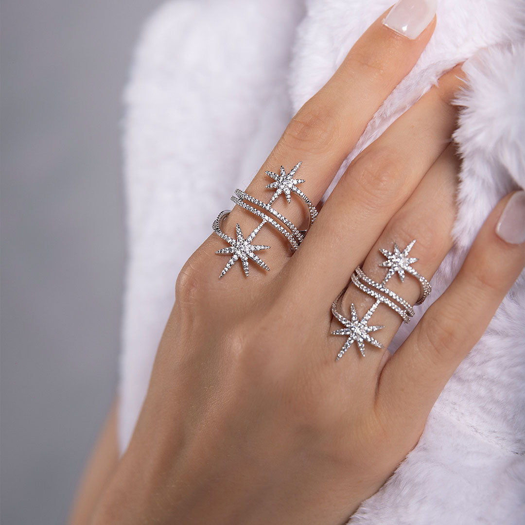 Hand wearing multiple APM MONACO silver star-shaped rings on a neutral background