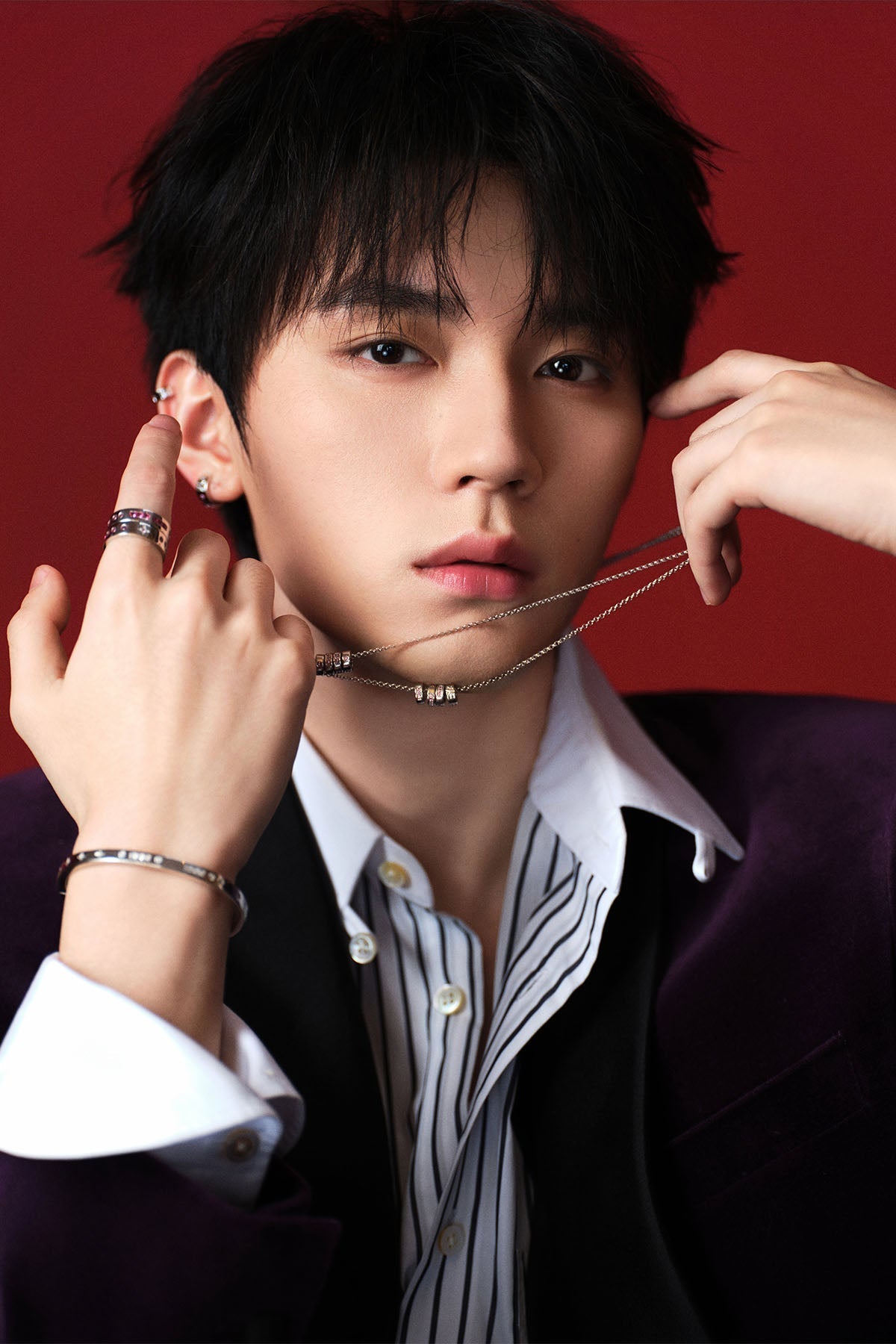 A model  adjusting a necklace against a red background