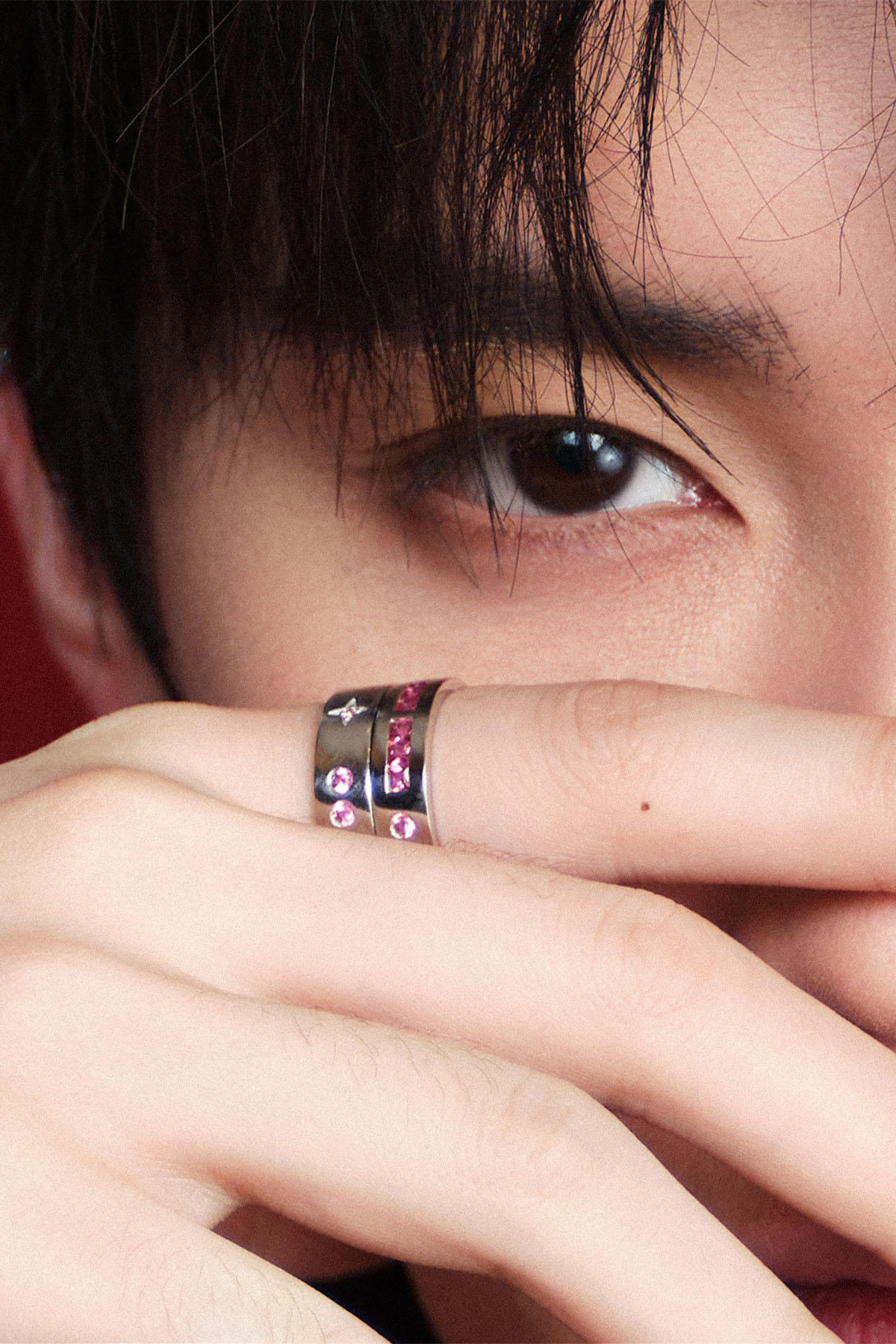 Close-up of a person wearing rings with colorful stones, covering part of their face.