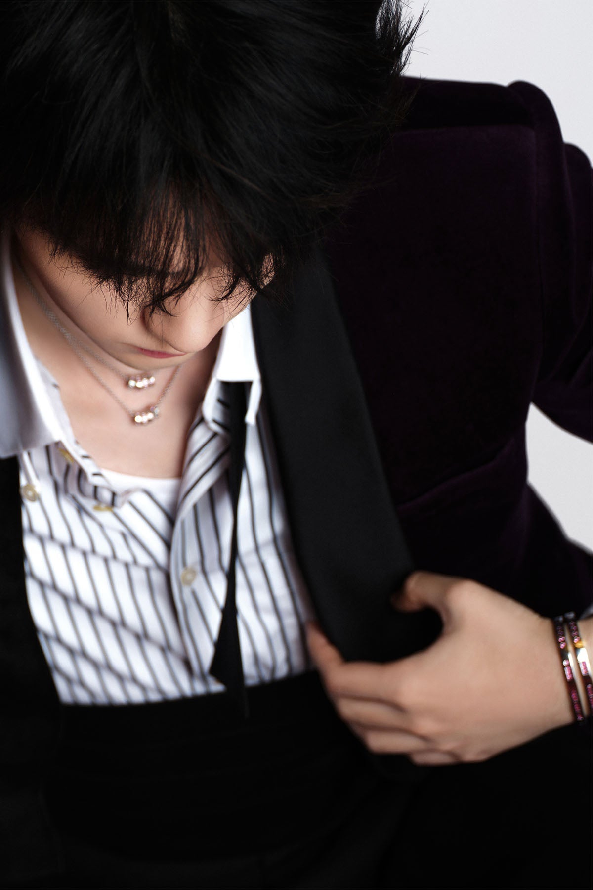 Model wearing a black suit jacket over a striped shirt with a white background