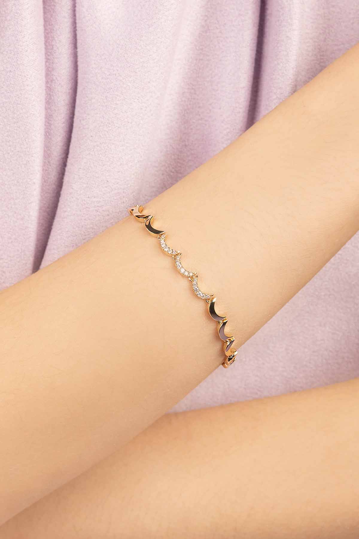 APM MONACO wavy gold bracelet on a wrist against a light pink fabric background