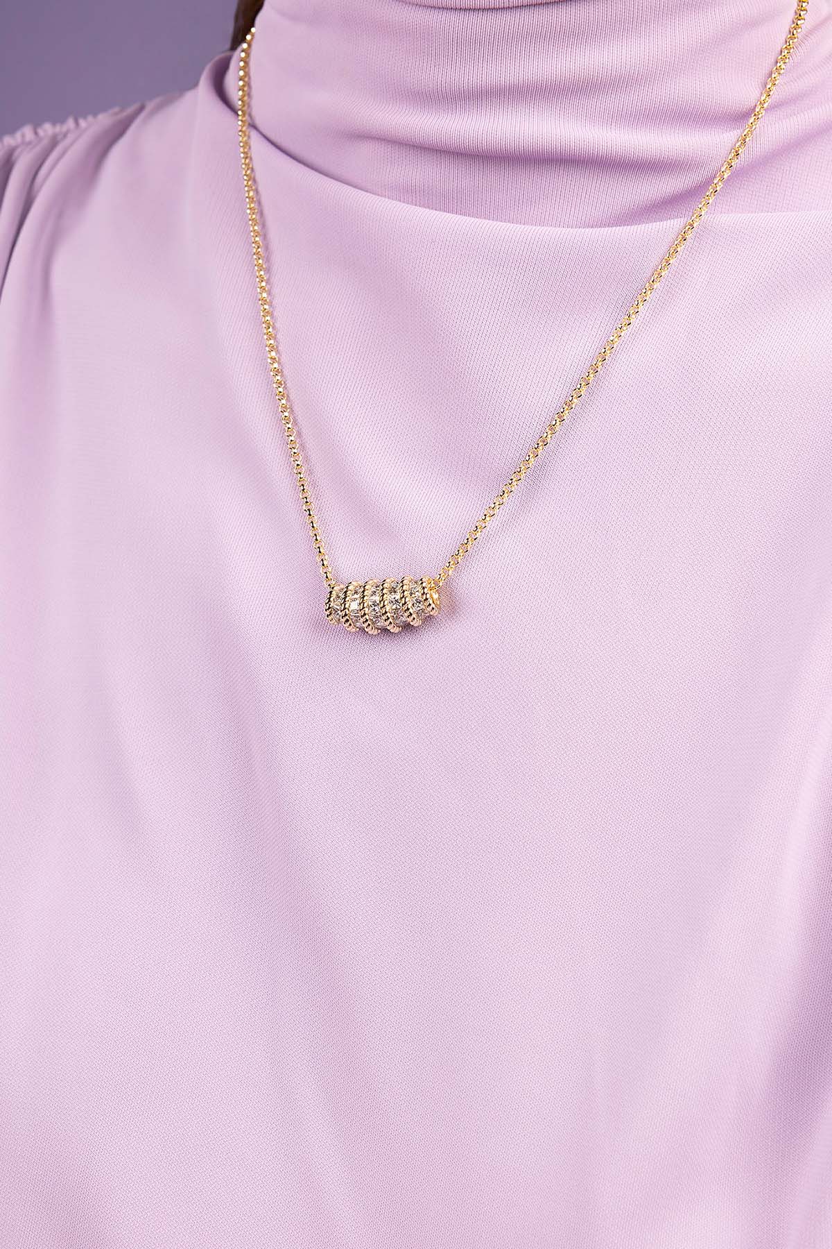 Gold necklace with a unique pendant on a person wearing a light purple top.